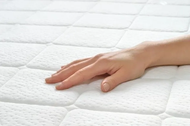 A person touching the bottom of a mattress.